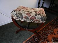 Side angle view showing curved wooden base and floral upholstered top with decorative studs.