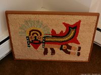Full view of framed textile wall art showing colorful stylized figure design on beige background