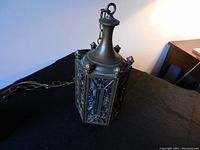 Overall view of the metal hanging lantern with decorative metal frame and colored glass panels. Shows top hanging loop and electrical cord.
