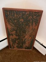 Angled view of the framed textured wood carving, showing the carved floral or botanical design with contrasting dark and wood grain areas.