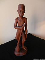 Front view of the wooden sculpture showing the boy holding a broom, standing on base.