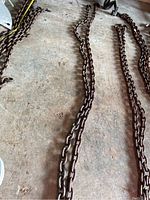 Photo showing two heavy-duty metal chains spread on a concrete floor with visible rust and wear.