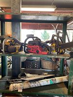 Three chainsaws on green metal shelving: Mastercraft yellow chainsaw 38 cm, red Homelite ZR chainsaw, and McCulloch 8 chainsaw