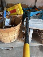 View of various clamps, yellow heavy-duty straps, wooden basket, and mop wringer with a long black and yellow handle on a shelf.