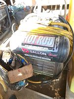 Side angle of Powerbuilt Hot Rod Series air compressor mounted on a hose cart with visible yellow coiled hose and part of the pneumatic bottle jack.