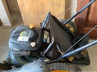 Full side top view showing the Craftsman mower with fabric grass collection bag and yellow adjustment knobs on handle; mower deck is green with black engine cover.