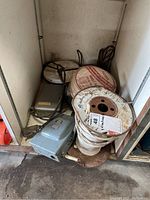 View of multiple reels of household electrical wire stacked in corner, showing white insulated cable and metal stands with some rust.