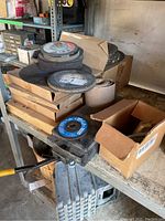 Stack of grinder blades and metal grinding wheels on a metal shelf with boxes.