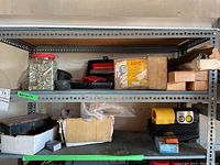 Metal shelves holding the lot items including boxes, jars with screws, a red book/manual, and a yellow and black device.