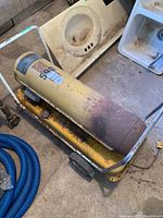 Side and top view of the industrial heater showing cylindrical yellow body on wheeled cart with rust and wear.