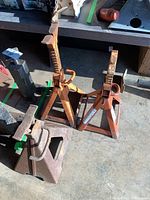 Three orange metal car jack stands with visible rust and wear, two adjustable with screw tops, one fixed base.