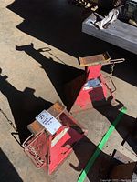 Two red steel jack stands placed on a concrete floor with some rust and chipping paint.