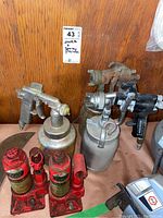 Overall front view of lot showing three paint sprayers and two hydraulic jacks on wooden surface.
