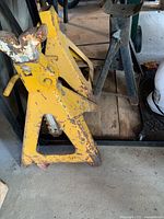 Yellow and black metal car jack stands with visible rust and wear on wooden floor.