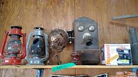 Full shelf shot showing 2 oil lanterns (red and gray), ceramic insulator, vintage telephone bar, Polaroid camera in box