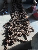 Two large, heavy rusted tractor tire traction chains laid on the floor showing full length and thickness.