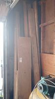 Stack of plywood sheets and wood folding door panels leaning against wall next to equipment
