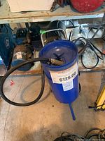 Photo shows the full blue 10 gallon sandblaster tank with attached hose and nozzle, placed on a shelf among other tools and equipment.