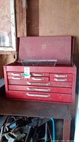 Red Mastercraft metal toolbox with flip-top lid and nine drawers, showing overall profile and condition.