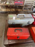 Photo showing the two tool boxes, one red metal box and one gray plastic box on a wooden surface.