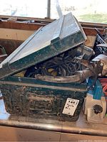 Green metal toolbox partially open with power tool cords inside