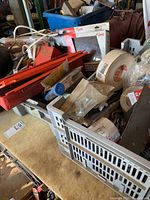 Overall view of plastic crates with hardware items, ratchet set red box, tape rolls, and electric cord on table surface