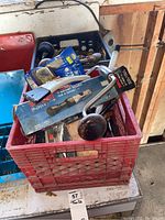 Full view of one red bin filled with assorted hand tools including a boxed ratchet wrench and hand drill