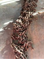 Two large, rusty metal traction chains laid out on a concrete floor, showing interconnected large oval and hook links with visible rust and weathering.