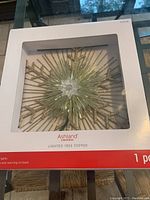 Photo of the Ashland branded box packaging showing the lighted tree topper with visible yellow and gold glittered star rays and central flower design.