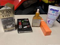 Five skincare products displayed: Olay Eyes cream in box, Cold Sore FX treatment box, Truly Anti-Aging Serum dropper bottle, Revolution Vitamin C cream box, Uremol 10 cream tube.