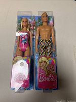 Two Barbie dolls in original packaging, showing front view of Beach Barbie and Beach Ken dolls.
