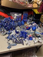 Blue and silver Christmas tree decorations spread on table including baubles, icicles, snowmen, stars, and packaged ornaments.