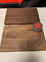 Photo shows two wooden charcuterie boards, one dark wood and one light wood, side by side on a flat surface with a tin of board butter placed on the lighter board.