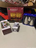Boxed 100 Light Star Set with large and small stars, 3 white ceramic tree candles in a clear box, and two boxed items including climbing Santa and LED bulb.
