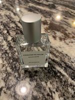 Clear glass rectangular perfume bottle with white label and silver cap on marble surface.