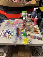 Overview photo of all craft items arranged on table including paints, ribbons, pom poms, paints, and glass jars