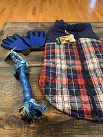 Photo of dog coat, grooming mitts, and rope toy laid out on wooden surface.
