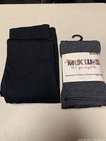 Two folded fleece lined leggings, one black and one heather grey in packaging, displayed on a surface.