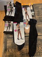 Top view of assorted hosiery items laid on floor showing multiple packages of black tights and hosiery with some open or damaged packaging.