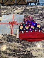 Christmas toque with LED lights on a granite countertop next to its giftable packaging featuring a white and light blue wrapping with red bow print.