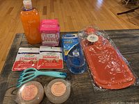 Overview of all items included in the relaxation and massage lot placed on a wooden surface showing foam bath bottle, boxed shampoo brush, memory gel insoles, hot water bottles, melatonin gummies, handheld massager, and salt bars.