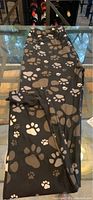 Full view of black leggings with large and small paw prints in brown and white laid flat on a glass table.