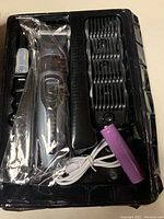 Pet hair trimmer in packaging showing purple rechargeable lithium battery, white charging cable, and black plastic guide combs