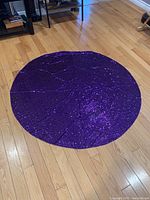 Full view of the 48 inch round purple sequin table cloth spread out on wooden floor, showing the shiny reflective surface and circular shape.