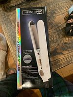 Box front showing InfinitiPro by Conair Compact Pro Ceramic Styler packaging, features listed including heat resistant travel pouch, dual voltage, 8 ft cord, 450°F heat, full size styling plates compact design.