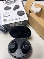 JVC Gumy Mini True Wireless black earbuds in charging case, showing box and damaged packaging materials around them.
