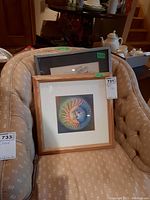 Two framed art pieces placed on an upholstered chair, showing colorful circular abstract designs.