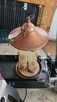 Copper top bird feeder with twin clear plastic tubes and circular metal base with feeding ports.