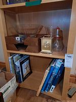 Shelf holding a glass bowl, glass vase, two wooden organizers, small square table clock, and a glass item resembling a seltzer bottle.