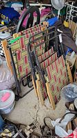 Six folding lawn chairs stacked together in a garage showing metal frames, patterned seats and backs, and wooden armrests.